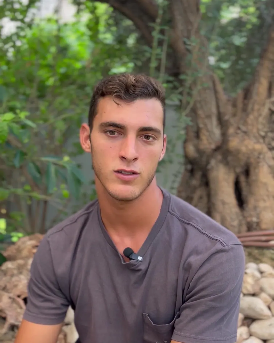 יובל פינקלס, מנחה התוכנית, יושב בחוץ ליד עץ זית